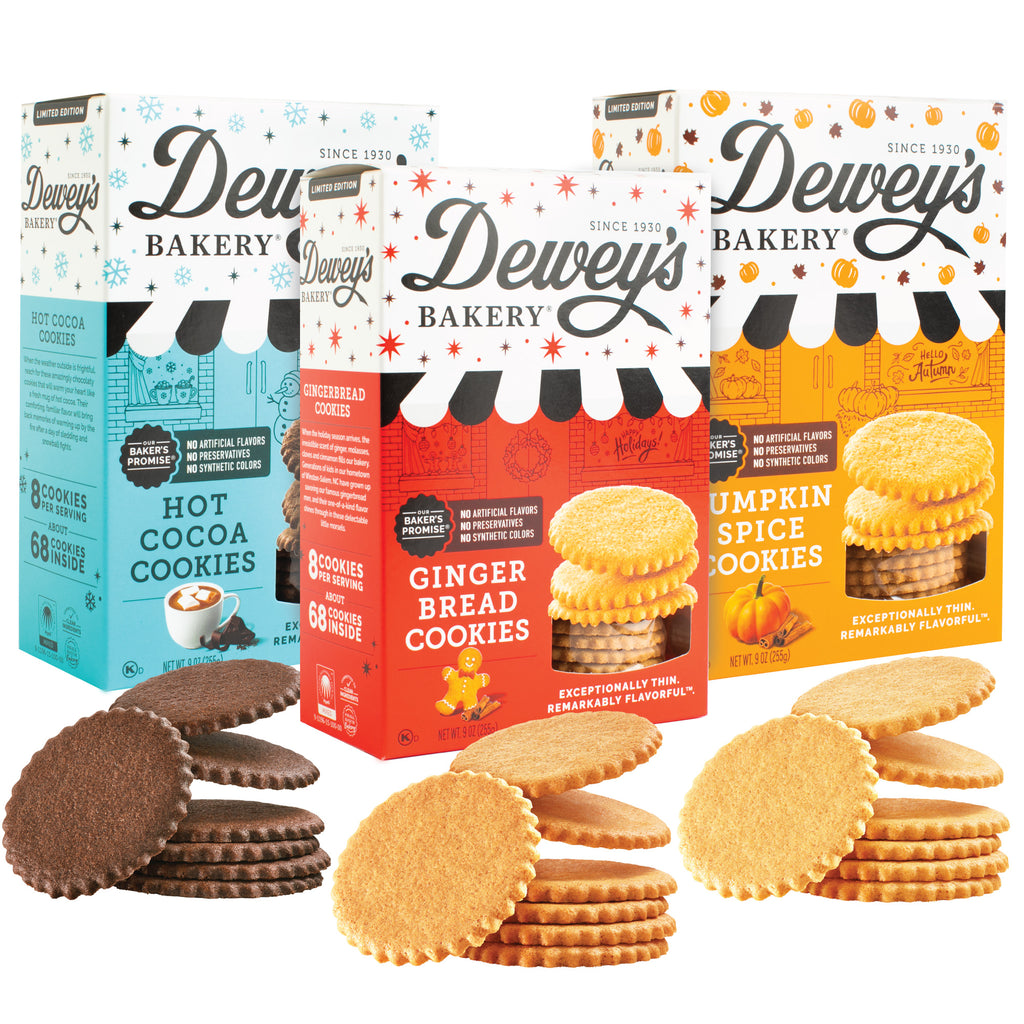 Three boxes of Dewey's Bakery cookies, featuring gingerbread, hot cocoa, and pumpkin spice varieties. The boxes are adorned with festive designs corresponding to each cookie flavor.